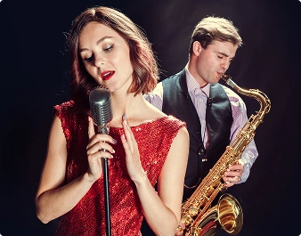 Kobieta w czerwonej sukience śpiewa do starego mikrofonu, a mężczyzna gra na saksofonie. Scena jest elegancka i przypomina atmosferę klubu jazzowego.