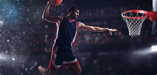 Koszykarz w powietrzu, gotowy do wsadu do kosza, ubrany w granatowo-czerwony strój. Jasne światła stadionu dodają emocji.
