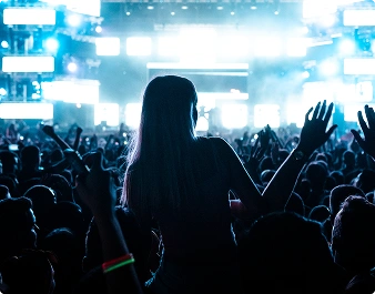 Tłum ludzi pod jasnymi neonowymi światłami sceny cieszy się energiczną atmosferą nocnego festiwalu muzycznego.