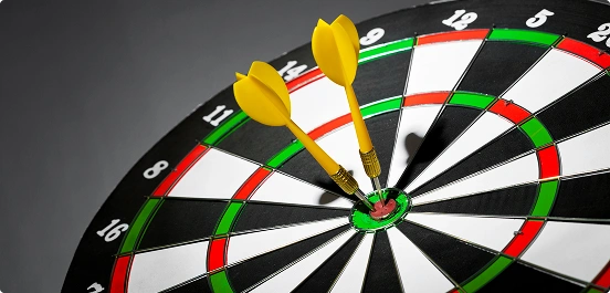 Tarcza do rzutek z dwoma żółtymi rzutkami w środku, otoczona naprzemiennymi zielonymi, czerwonymi, czarnymi i białymi segmentami. Wysoki kontrast i wyrazisty ton.